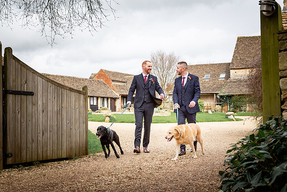 Two Grooms share a moment with their pet dogs following their same sex wedding at Great Tythe Barn in Tetbury